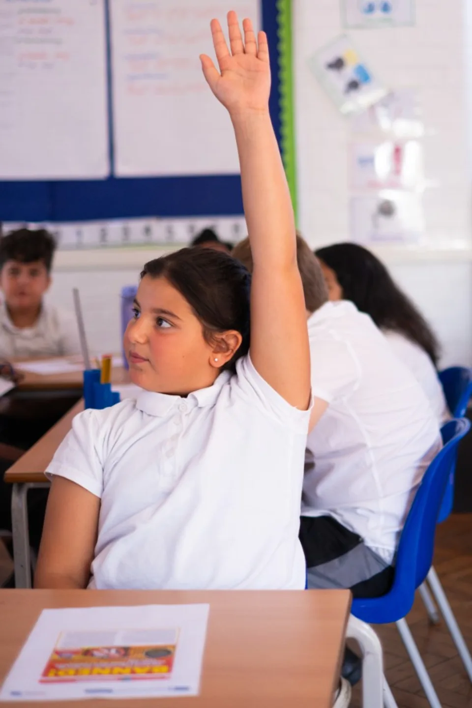 A pupil raising her hand to contribute to a classroom discussion