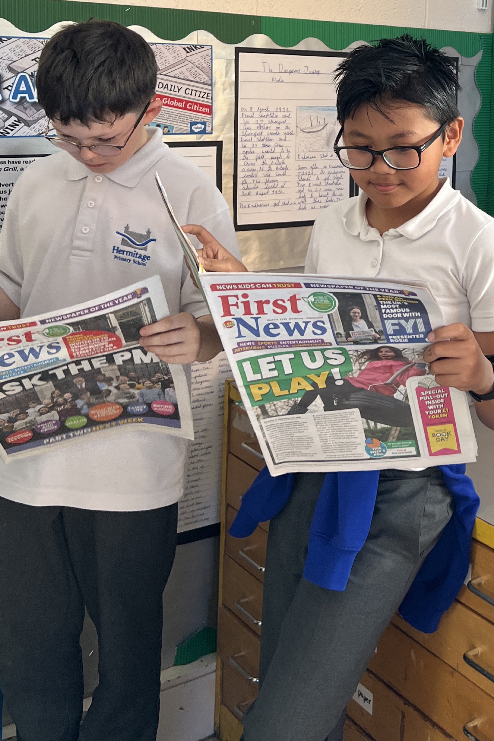 Two pupils reading copies of First News in a classroom