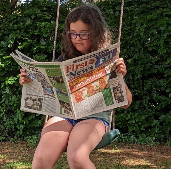 An image of a young girl on a swing reading First News