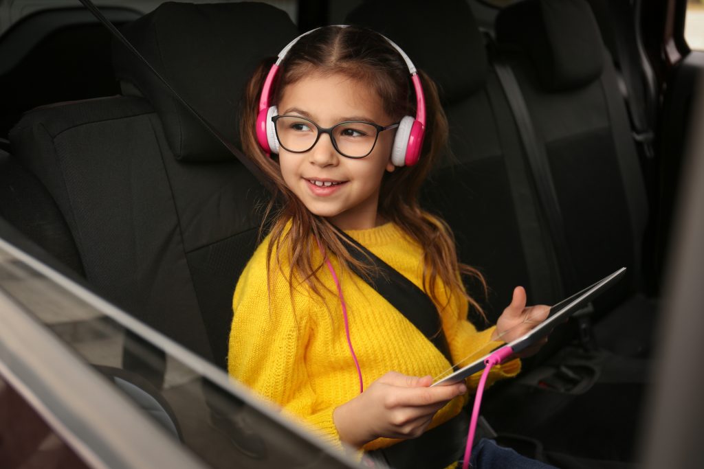A young girl holding a tablet whilst she is wearing headphones in a car
