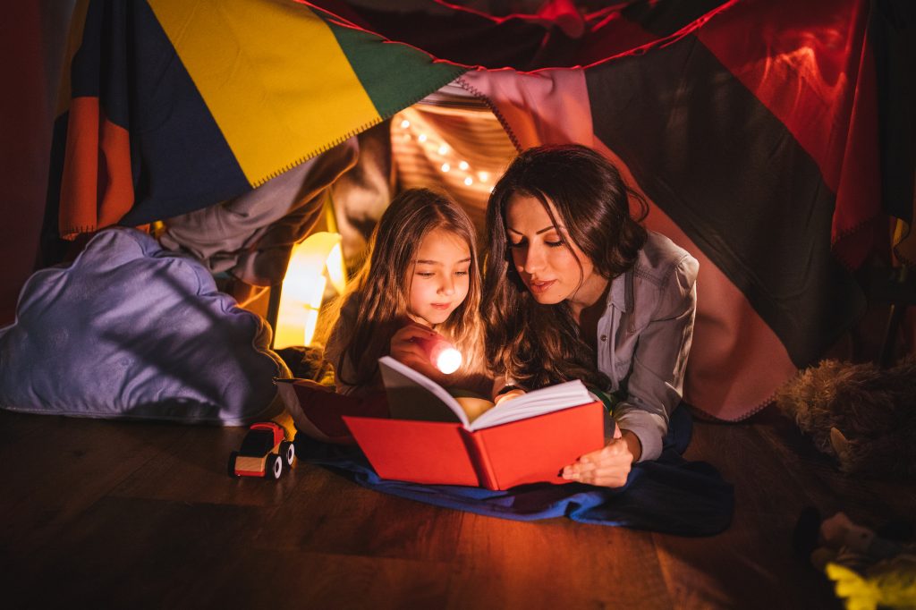 An older woman reading alongside a younger girl whilst she holds a flashlight