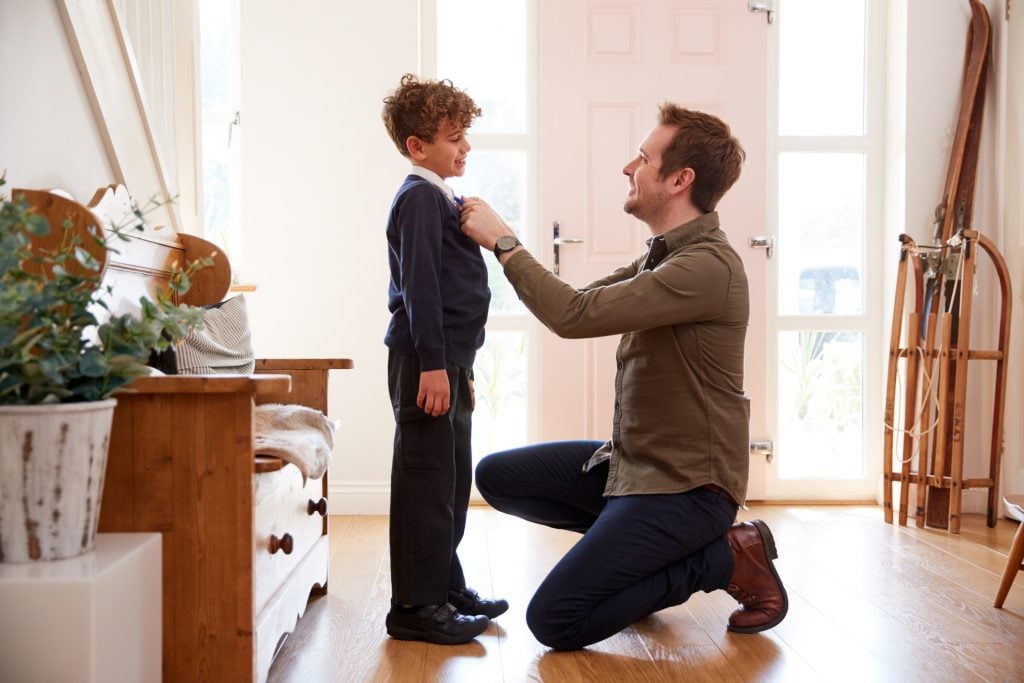Single Father At Home Getting Son Wearing Uniform Ready For First Day Of School