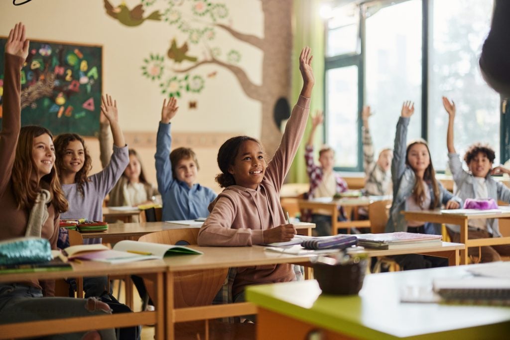 Large group of happy elementary students know the answer on a class in the classroom. Focus is on black girl.